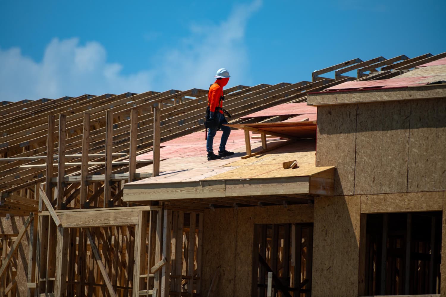 Summit Shield worker on new roof construction framing against blue sky